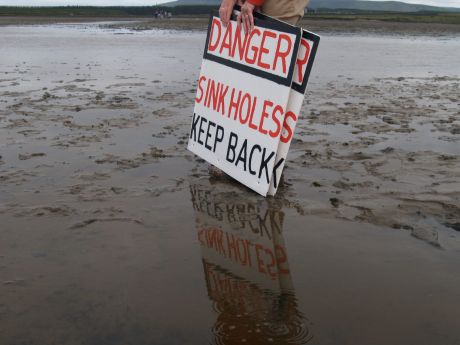 Bubbling in the water in the foreground while people raise warning signs in the background of photo
